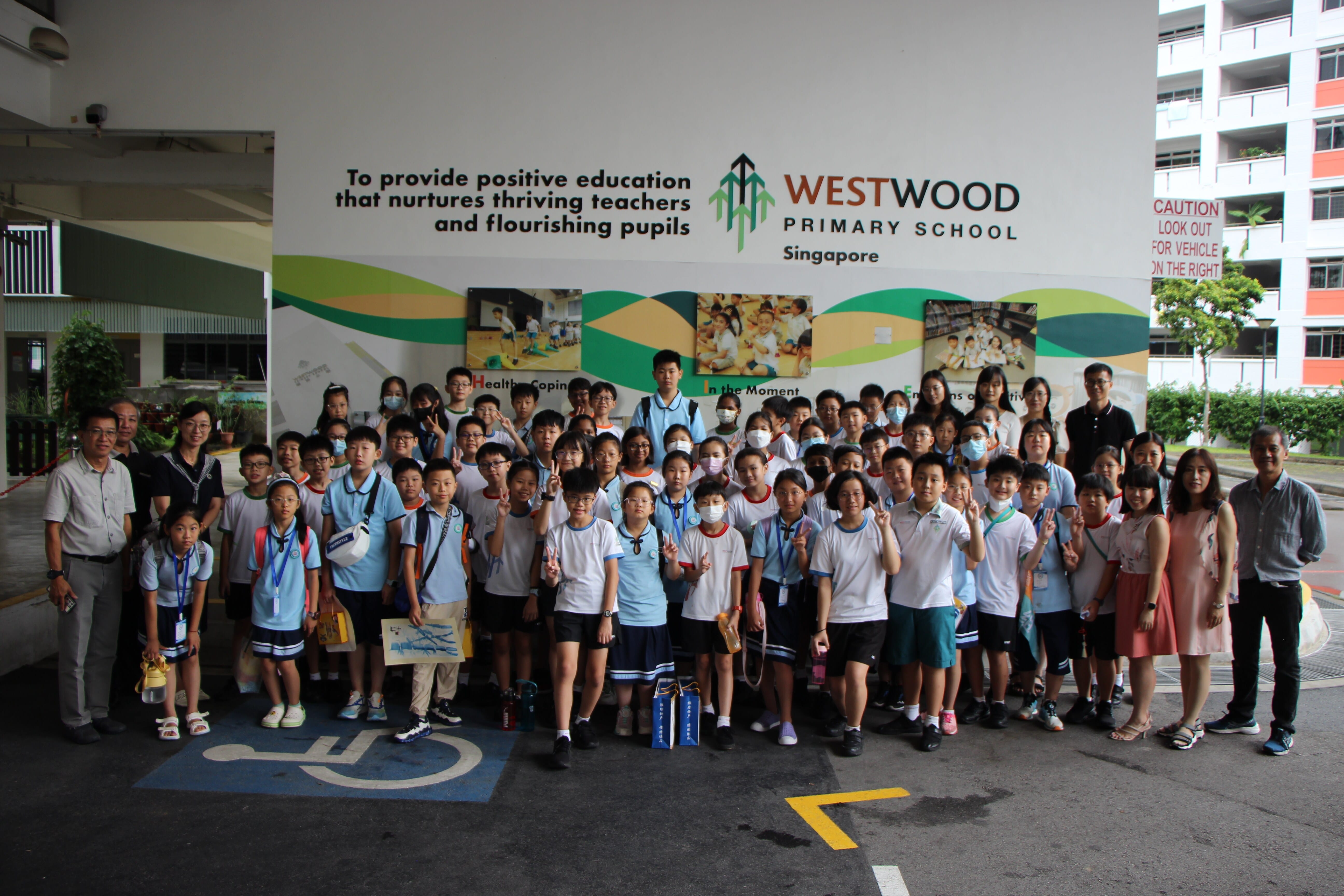 Large group of students and teachers posing in front of Westwood Primary School Singapore wall mural.